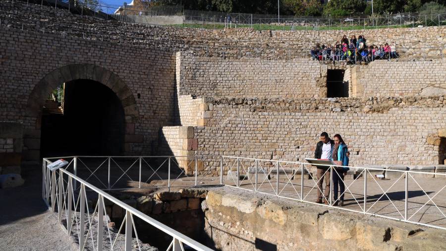 Dos turistes visitant l'amfiteatre romà de Tarragona amb un grup d'escolars assegut a la graderia. FOTO: ACN