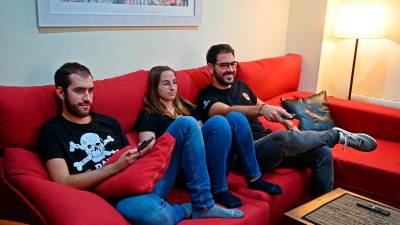 Marta Fàbregas, junto a sus dos compañeros de piso en la Part Alta, sentados en el sofá viendo la televisión. Foto: Alfredo González