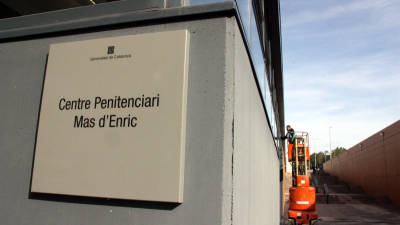 Primer pla del cartell del centre penitenciari de Mas d'Enric, amb un operari netejant vidres de l'entrada principal al fons, el 20 de novembre del 2015. ACN