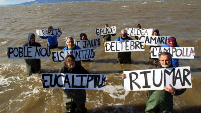 Diversos membres de les diferents entitats dins de l'aigua amb cartells dels pobles del Delta de l'Ebre, simbolitzant el seu enfonsament. Foto: ACN