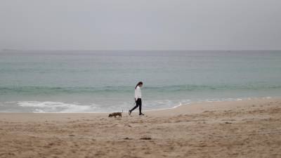 Una mujer y su perro paseaban este jueves por la playa del Orzán, en A Coruña, con el cielo cubierto por la niebla. Sin perspectiva de lluvias a corto plazo, en el arranque otoñal más cálido de la historia, un déficit anual de precipitación cercano al 11 por ciento y embalses en niveles de agua agónicos agravan la fuerte sequía que arrastra España en los últimos años. Foto: EFE