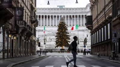 Un hombre cruza una calle con el telón de fondo del árbol de Navidad en la Piazza Venezia y el Monumento Nacional Víctor Emmanuel II durante el cierre de Navidad en Roma, Italia, el 25 de diciembre de 2020.&nbsp;EFE / EPA / ANGELO CARCONI
