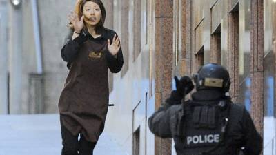 Una empleada abandona la cafetería donde trabaja y que un hombre armado tiene tomada desde primeras horas de la mañana en Sídney. Foto: EFE
