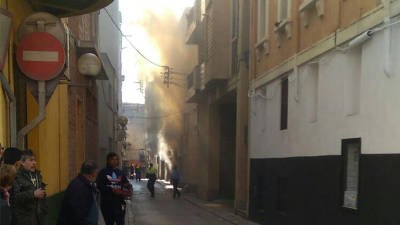 Pla obert del carrer on, al fons, es veu el fum d'un foc que ha cremat la primera planta d'una casa deshabitada a Valls. Foto: ACN