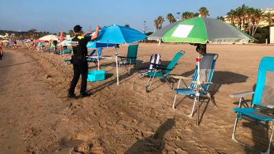 Un agente de la Policía Local coloca en una sombrilla el aviso de que la ‘reserva’ en la playa está prohibido en La Pineda. FOTO: DT
