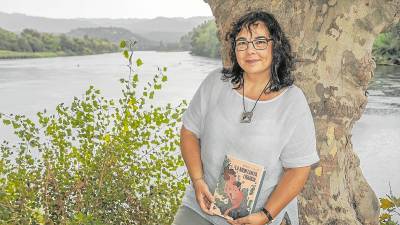 L’ebrenca d’adopció Mercè Falcó amb la novel·la ‘La muntanya líquida’ a Xerta, amb el riu Ebre darrere. Foto: Joan Revillas