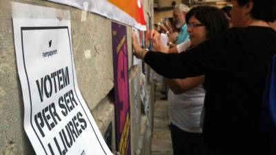 Un cartell a favor de votar l'1-O en primer terme i al fons gent penjant cartells a la façana de l'Ajuntament de Tarragona, en un acte de l'ANC i Òmnium a la plaça de la Font. Imatge del 24 de setembre del 2017. Foto: ACN