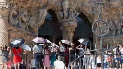 Un grupo de turistas se protege del sol en una de las puertas de la Sagrada Familia de Barcelona. FOTO: EFE
