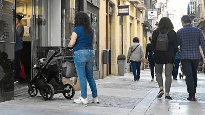 Una mujer con un carrito de bebé camina en el centro de Reus, cerca de un establecimiento junto a la Plaça del Mercadal. FOTO: Alfredo González