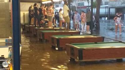 Varias personas subidas a las mesas de billar en una terraza inundada de la calle Carles Buïgas, este pasado sábado. FOTO: FACEBOOK