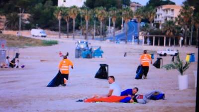 Trabajadores limpiando y personas que han prolongado la fiesta en la playa. Foto: Pere Ferré