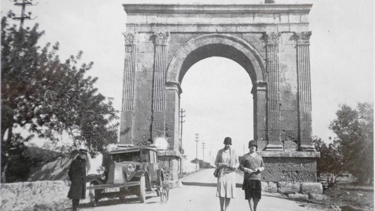 Dos mujeres pasean ante el Arc de Berà mientras su chófer las espera. Foto: ‘Tarragona, segle XX a través de les postals’