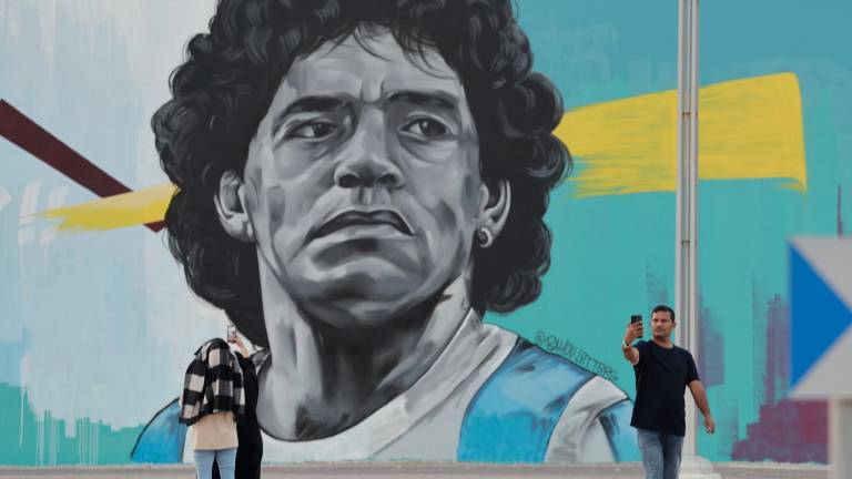 Ciudadanos cataríes fotografían un mural del exjugador argentino Diego Armando Maradona, enfrente del estadio Al Khalifa de Doha, Catar, este viernes. EFE/Antonio Lacerda