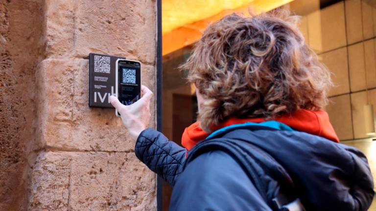 Una persona escanejant el QR de la nova placa instal·lada a l’exterior de la joieria ‘Personal’ de Tarragona i que forma part del projecte ‘Empremtes del passat’. Foto: ACN