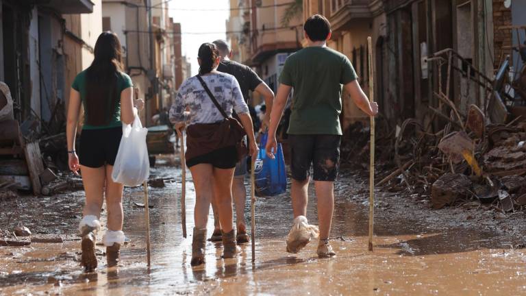 Varias personas caminan entre el lodo acumulado en las calles a causa de las intensas lluvias caídas por la fuerte dana, este jueves en Catarroja. Catarroja, una de las localidades afectadas por la dana que asoló este martes la provincia de Valencia, se afana por restablecer los suministros cortados a consecuencia del temporal y en ofrecer ayuda humanitaria a los vecinos. Foto: EFE
