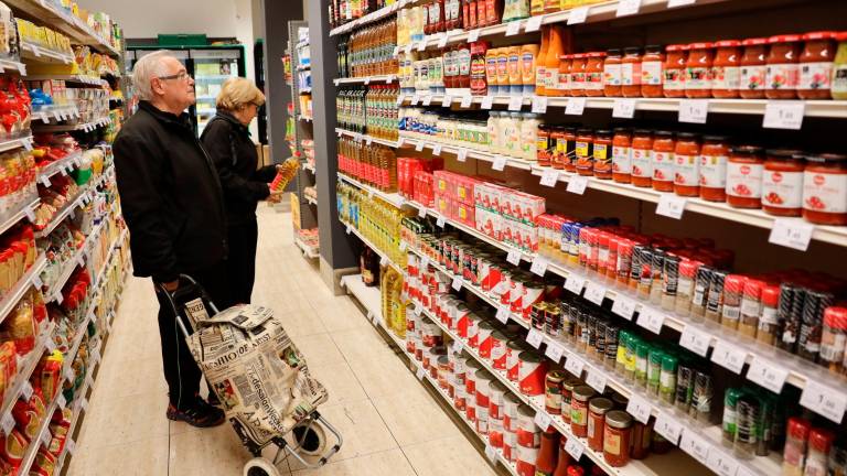 Dos personas ante la estantería de un super. Cada vez más, los clientes miran los precios y se decatan por las marcas blancas. FOTO: Alba Mariné