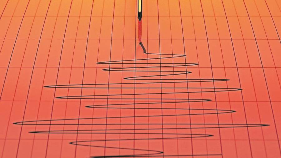 Un primer plano de una aguja de máquina sismógrafo dibujando en papel cuadriculado que representa la actividad sísmica y sísmica