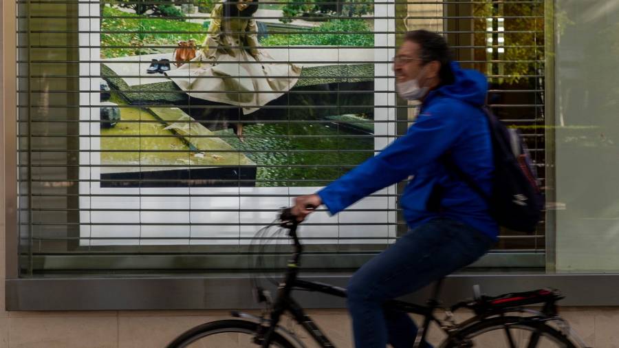 Un hombre pasa en bici ante un comercio cerrado. FOTO: EFE