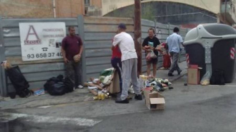 Diversas personas se disputan en El Vendrell frutas y verduras de un contenedor. Foto: DT
