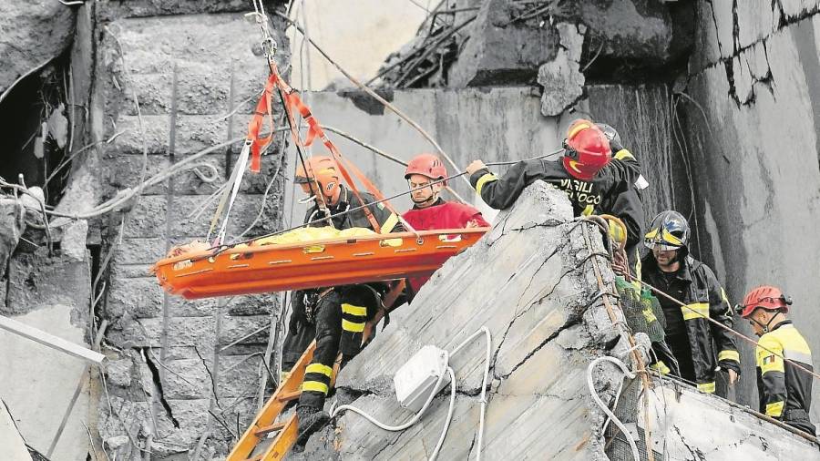 Los bomberos rescatan a una persona. Algunos veh&iacute;culos quedaron ocultos entre los escombros y otros, los de mayor tonelaje, terminaron en un riachuelo que pasa justo por debajo del puente. FOTO: EFE