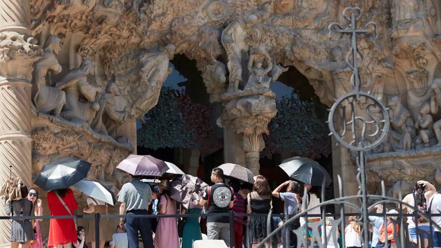 Un grupo de turistas se protege del sol en una de las puertas de la Sagrada Familia de Barcelona. FOTO: EFE