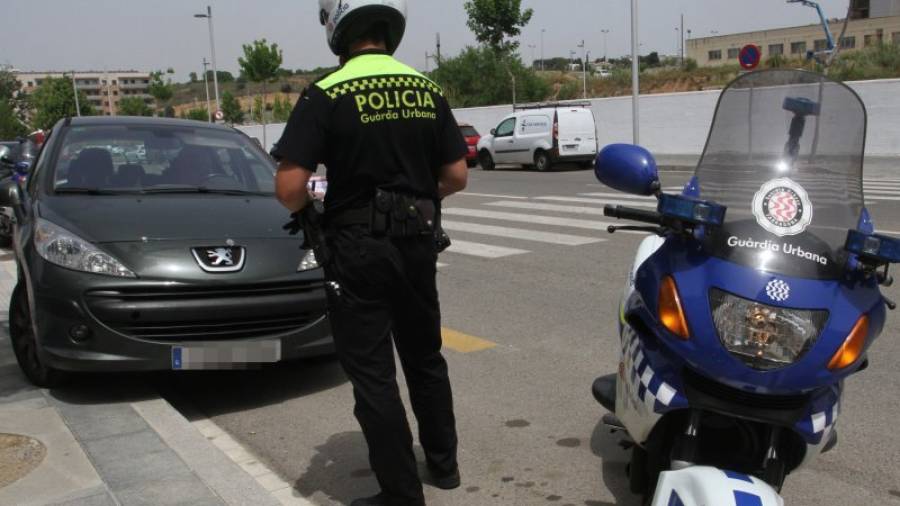 Un agente de la Guàrdia Urbana multando un vehículo estacionado encima de la acera. Foto: Lluís Milián