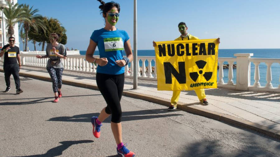 Una noia corre amb la cara pintada durant la cursa a l'Ametlla de Mar mentre un noi sosté una pancarta en contra de les nuclears. Foto: ACN