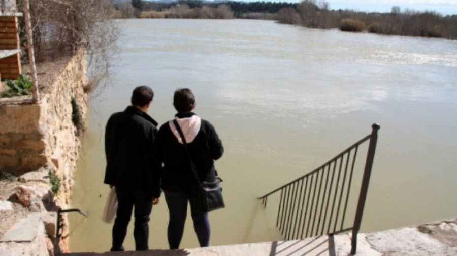 Dos veïns de Miravet observen la crescuda de l'Ebre en el punt que pot començar a inundar la façana fluvial. Foto: ACN
