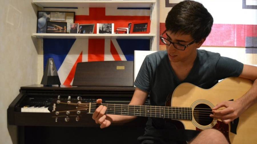 El vallenc Jaume Sanz tocant la guitarra a la seva habitació, on enregistra les cançons. Foto: Montse Plana