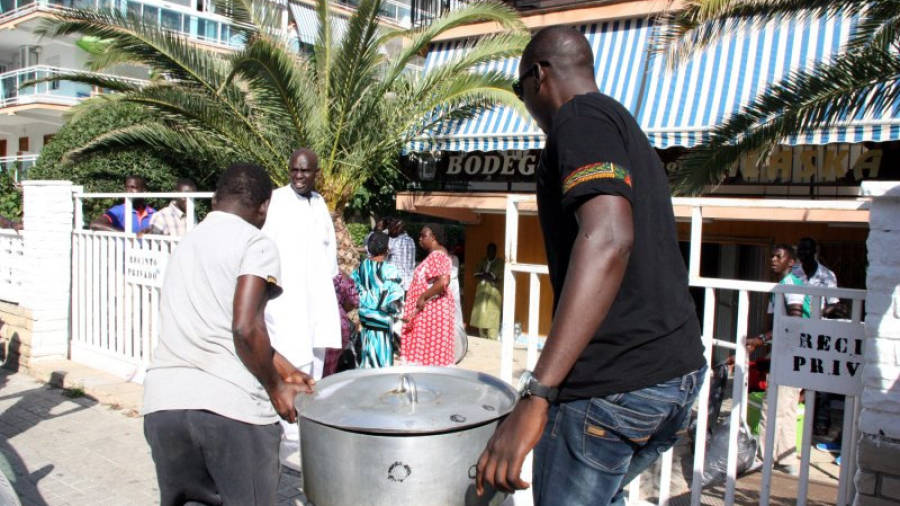 Dos homes carregant una olla amb menjar per compartir amb la resta de senegalesos aplegats en un local de Salou. Foto: ACN
