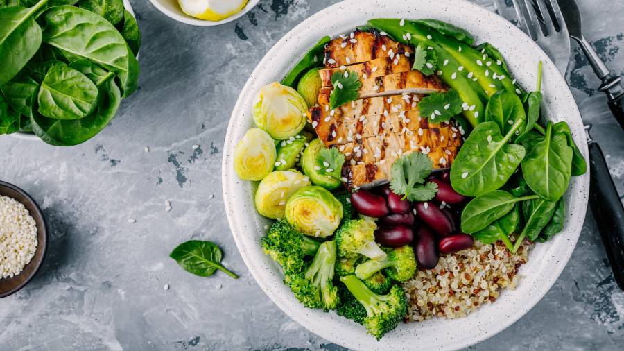 Healthy buddha bowl lunch with grilled chicken, quinoa, spinach, avocado, brussels sprouts, broccoli, red beans with sesame seeds