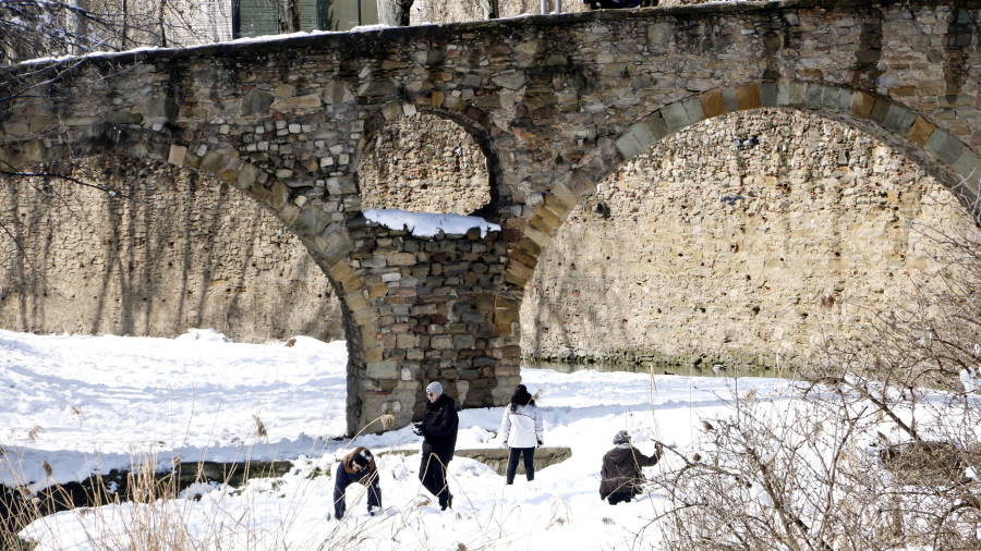Un grup de joves juga amb la neu que hi ha a la llera del riu M&eacute;der de Vic i es fan fotografies