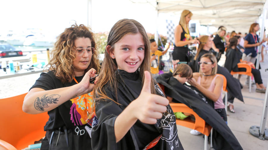 Un niña muestra su satisfacción mientras una peluquera le hace un corte de pelo. FOTO: ALBA MARINÉ