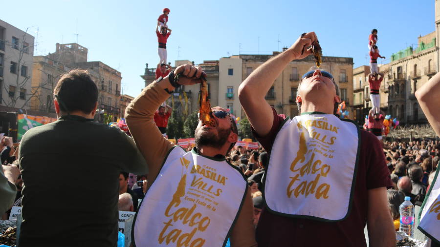 Dos participants del concurs de menjar cal&ccedil;ots degusten una ceba dol&ccedil;a mentre al darrere aixequen pilars durant la Gran Festa de la Cal&ccedil;otada de Valls. FOTO: ACN