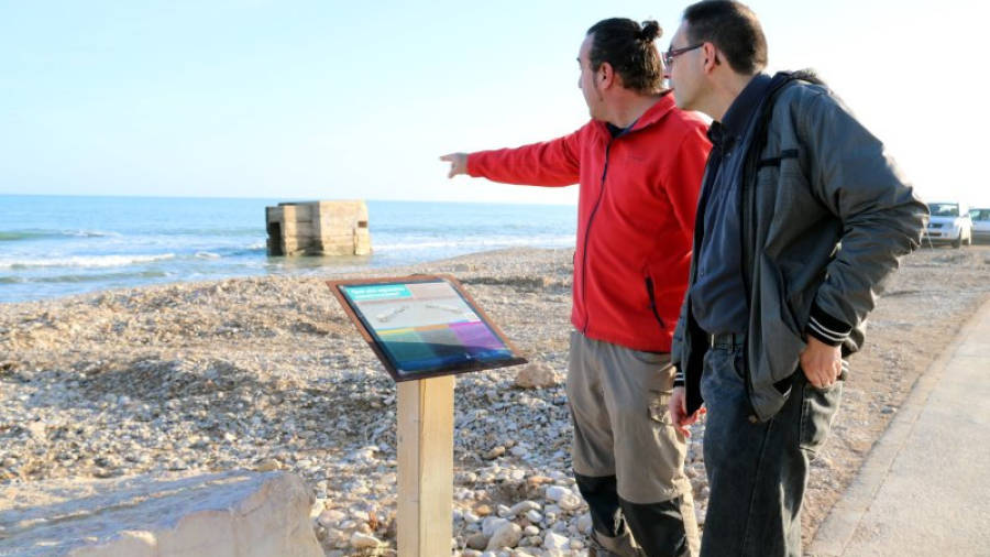 El president de l'Associació Cultural Lo Rafal, Joaquim Buj, i l'arqueòleg, Damià Grinyó, observant un dels nius de metralladora de la platja de l'Estanyet, davant del cartell informatiu d'aquests elements