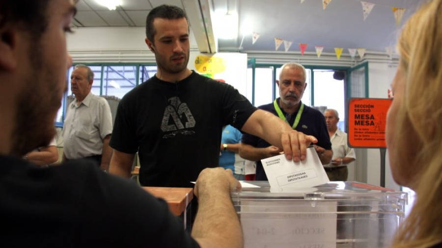 Un home diposita el seu vot a l'urna davant la mirada dels membres de la mesa en un col·legi electoral. ACN