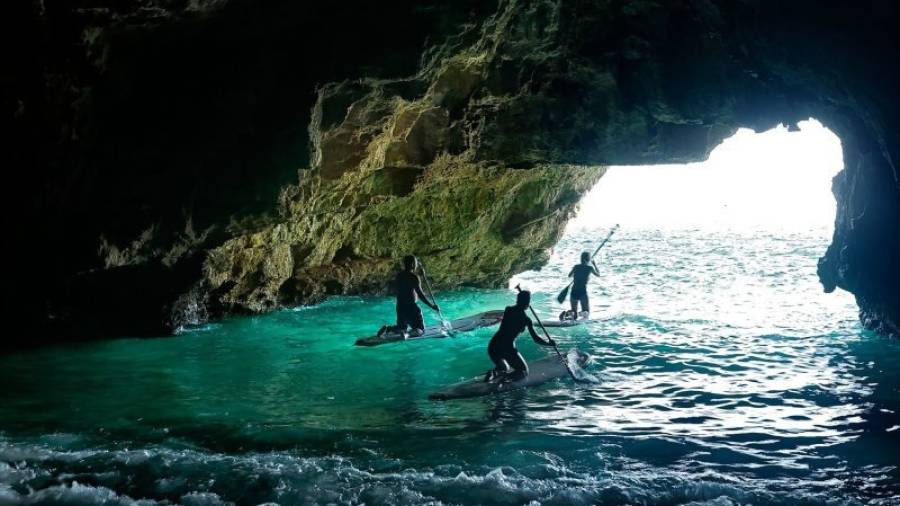 Tres jóvenes salen de la gruta subidos en una tabla de paddle surf. Foto: Cedida
