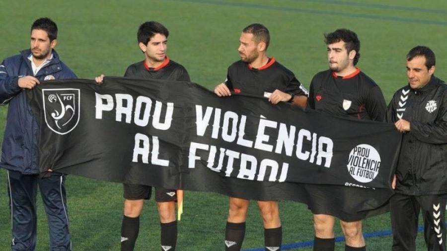 El árbitro tarraconense Daniel López (centro), agredido recientemente en Lleida, sostiene una pancarta de repulsa a la violencia. Foto: DT