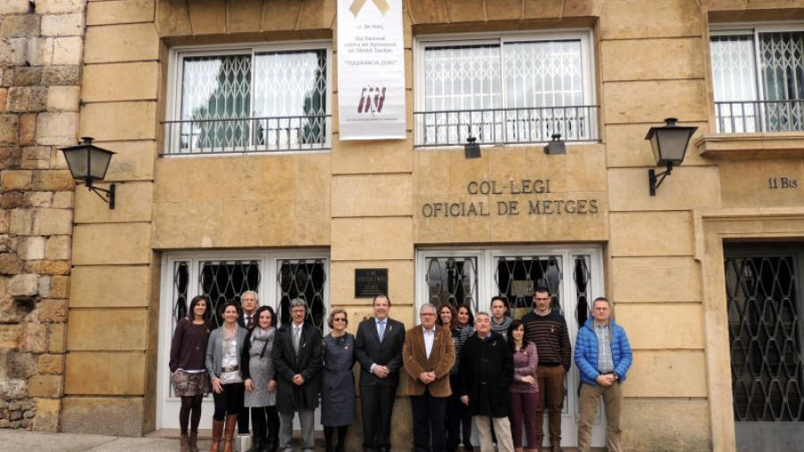 Un grup de metges sota la pancarta amb el llaç daurat que ha penjat el Col·legi Oficial de Metges de Tarragona a la seva façana per demanar que no es produeixin més episodis de violència. Foto: ACN