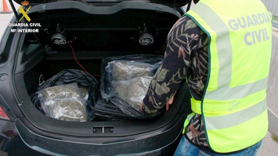 Un agente de la Guardia Civil mostrando dos bolsas de marihuana localizadas en un coche que habría huido de un control en la A-27.