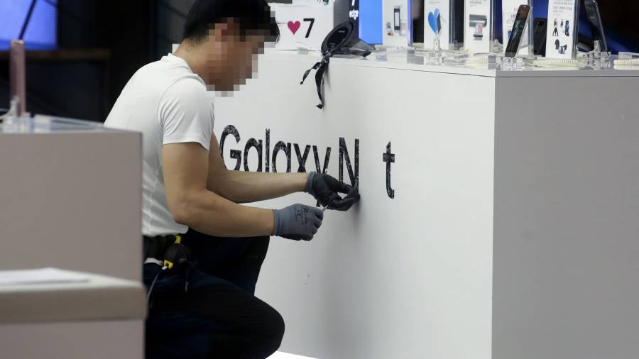 Un empleado quita las marcas publicitaria de Galaxy Note 7 de una tienda en SeÃºl. FOTO: EFE