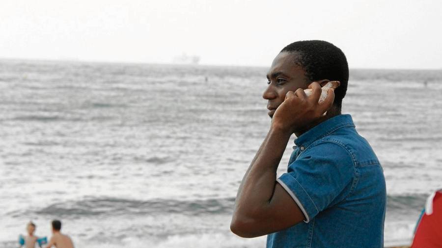 Peter, un refugiat nigerià, escoltant un dels cargols de mar a la platja de Sant Sebastià de Barcelona. acn