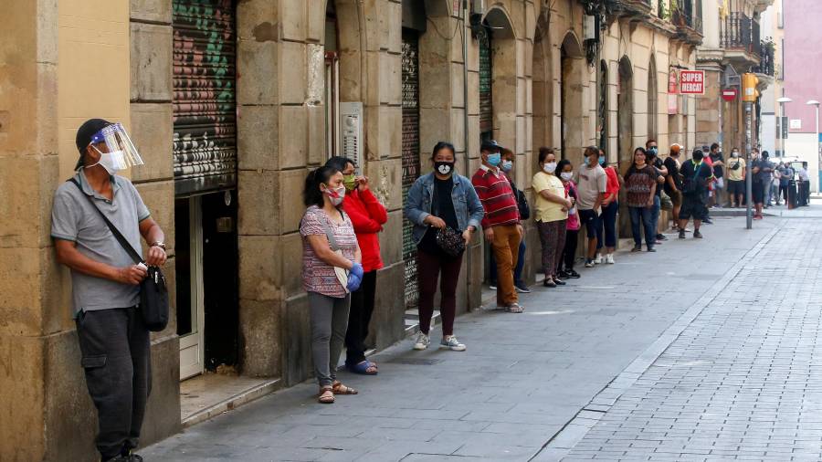 Imagen de varias personas en Barcelona haciendo cola para recibir alimentos. EFE