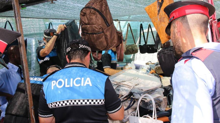 Dos agentes, uno de los Mossos y otro de la Policía Local comprueban los datos de un puesto en el mercadillo semanal de La Pineda (Vila-seca). FOTO: Alba Mariné