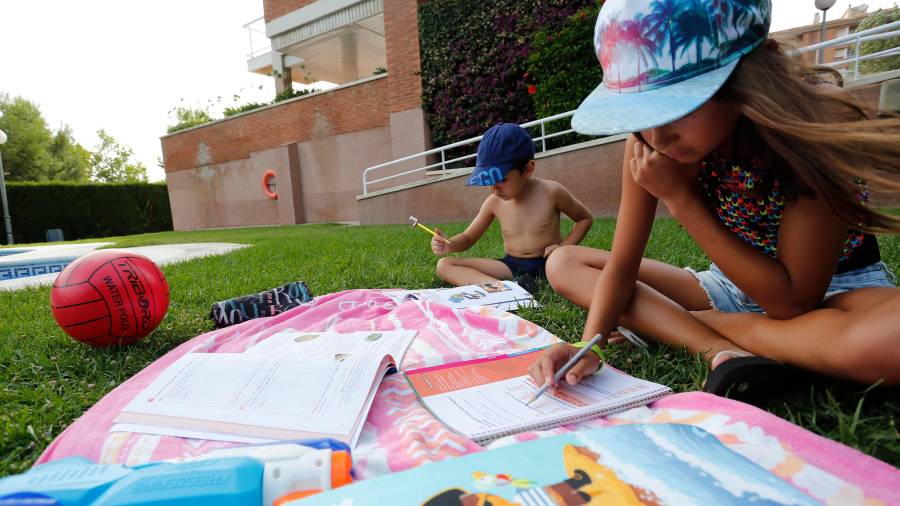 Dos niños hacen deberes durante sus vacaciones, en la piscina. Foto: PERE FERRÉ
