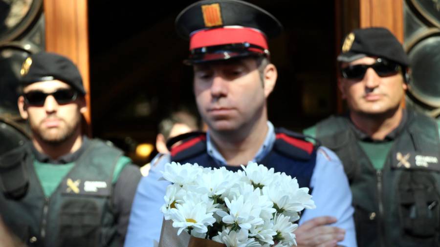 Un ramo de flores blancas en primer término ante un agente de los Mossos, que luego lo ha cogido, y dos de la Guardia Civil de fondo, frente a la sede de Economía