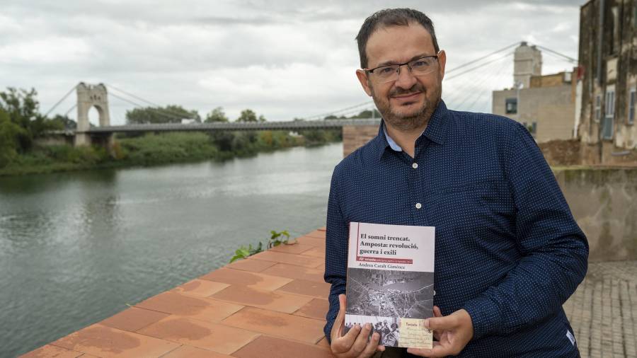 Andreu Caralt amb el llibre i el pont Penjant d’Amposta de fons. FOTO: JOAN REVILLAS