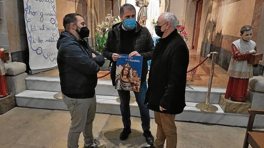 El regidor Marc Ayala, mossèn Joan Àguila –amb el cartell de la Verge– i el membre de la comissió participativa d’Actes Religiosos Albert París, ahir davant de la Mare de Déu de la Candela. FOTO: ÀNGEL JUANPERE
