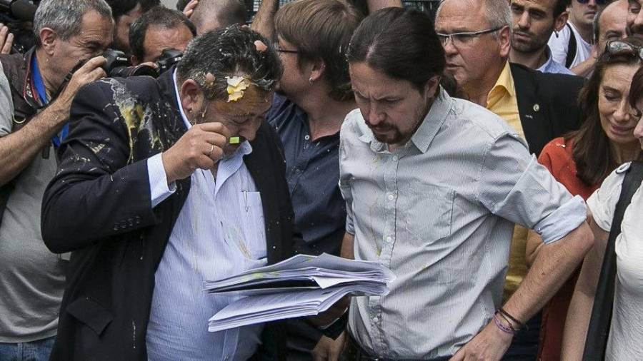 Julio Sanz, presidente de la Federación Profesional del Taxi, recibe el impacto de un huevo mientras conversa con el líder de Podemos, Pablo Iglesias. EFE/Santi Donaire