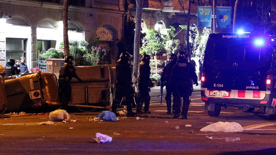 Pla general d'agents antidisturbis dels Mossos d'Esquadra retirant contenidors tombats al mig del carrer a Barcelona durant els aldarulls posteriors a la manifestació del 25 de març